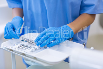 Mid section of nurse picking up dental tools from tray