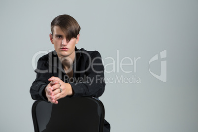 Androgynous man sitting on chair against grey background