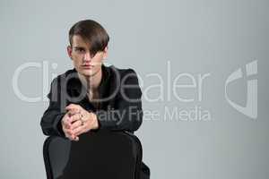 Androgynous man sitting on chair against grey background
