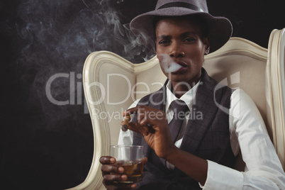 Androgynous man smoking cigar while while sitting on a chair