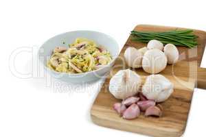Vegetables with garlic on cutting board by pasta in bowl