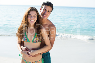 Happy man embracing girlfriend standing on shore at beach