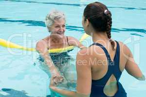 Female coach helping senior woman in swimming pool