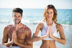 Portrait of young couple meditating while sitting on shore