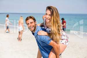 Man piggybacking girlfriend against friends at beach