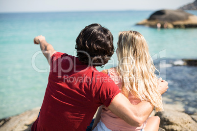 Man pointing towards sea while sitting with woman