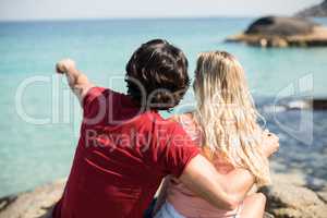 Man pointing towards sea while sitting with woman
