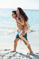 Side view of happy man piggybacking girlfriend on shore