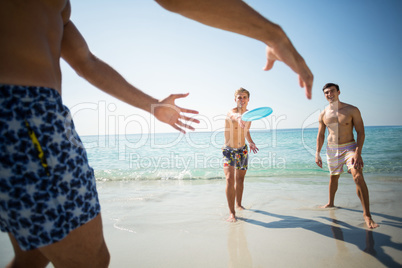 Male friends playing frisbee on shore