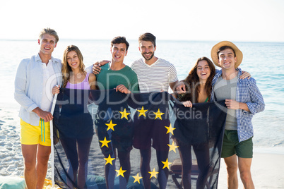 Friends holding European Union flag on shore at beach