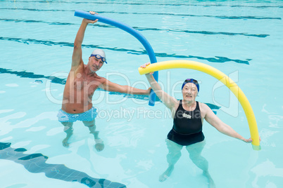 Senior couple exercising with pool noodle in swimming pool