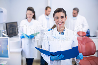 Smiling dentist holding file at dental clinic