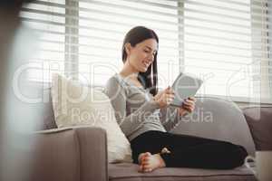 Smiling woman holding tablet while sitting on sofa
