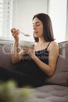 Smiling woman eating breakfast while sitting on sofa