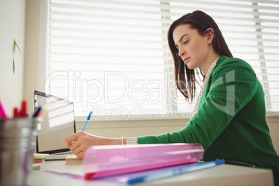Side view of woman writing while sitting at table