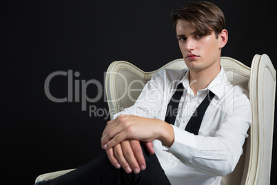Androgynous man sitting on chair against black background