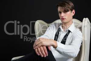 Androgynous man sitting on chair against black background