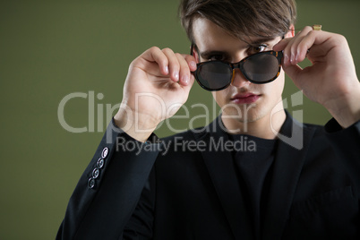 Androgynous man in sunglasses posing against green background