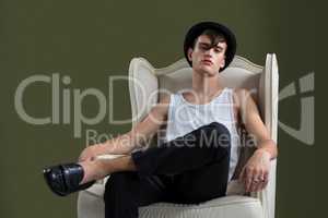 Androgynous man sitting on chair against green background