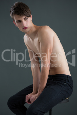 Shirtless androgynous man sitting on stool
