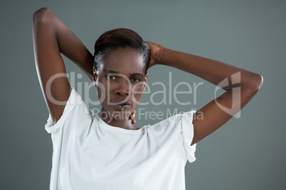 Androgynous man posing with hands behind head against grey background