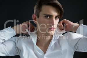 Androgynous man adjusting his collar against black background