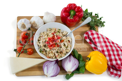 Overhead view of pasta served in bowl amidst vegetables on cutting board