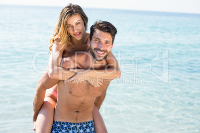 Happy man piggybacking girlfriend on shore at beach
