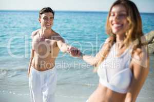 Woman holding boyfriend hand while standing on shore