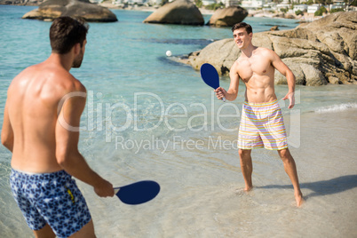 Male friends playing matkot on shore at beach