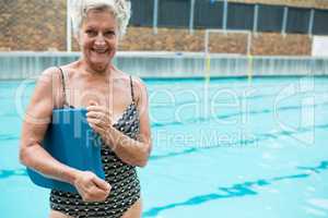 Smiling senior woman holding kickboard at poolside