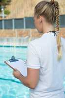 Female coach writing on clipboard at poolside