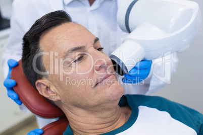Mid section of dentist examining a male patient with dental tool