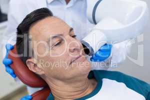 Mid section of dentist examining a male patient with dental tool