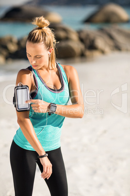 Young woman using smartphone on armband at beach