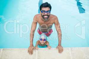 Portrait of father and son wearing swimming goggles in pool