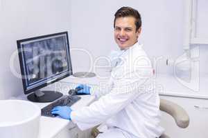 Portrait of happy dentist examining x-ray report on computer