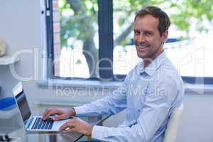 Portrait of smiling dentist working on laptop