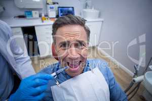 Dentist injecting anesthetics in scared male patient mouth