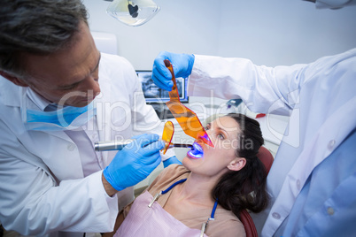 Dentists examining female patient with dental curing light