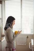 Woman using smart phone while standing against window