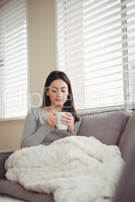 Woman holding cup while sitting on sofa