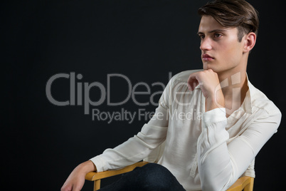 Androgynous man sitting on chair with hand on his chin