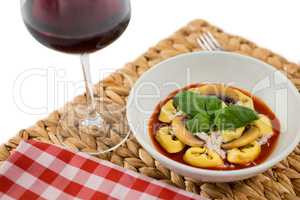 Close of cooked tortelloni in bowl on napkin by wineglass