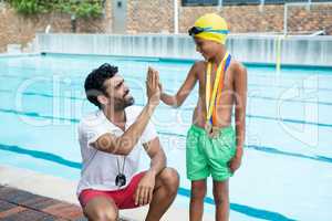 Boy giving high five to coach near poolside