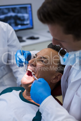 Dentists examining a male patient with tools