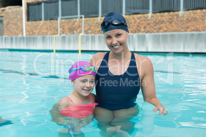 Portrait of female instructor and young girl standing in pool