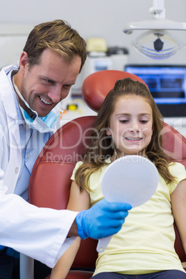 Dentist showing mirror to young patient in dental clinic