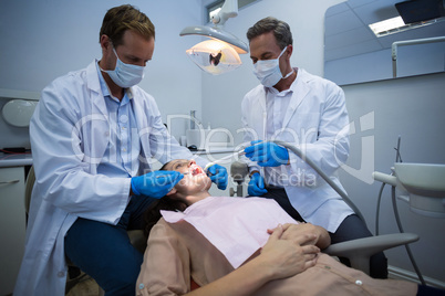 Dentists examining a female patient with tools