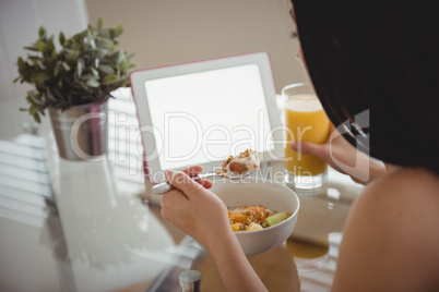 Woman eating breakfast while using laptop